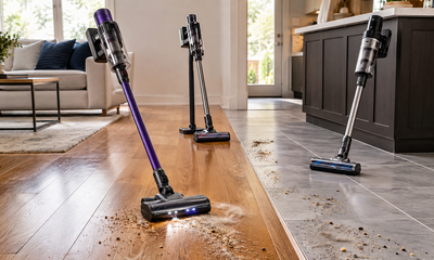 Cordless vacuums cleaning wood and tile floors with visible dust, pet hair, crumbs, and debris along grout lin