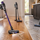 Cordless vacuums cleaning wood and tile floors with visible dust, pet hair, crumbs, and debris along grout lin